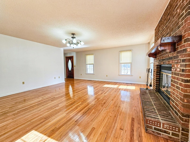 unfurnished living room featuring a brick fireplace, baseboards, a chandelier, light wood-style flooring, and a textured ceiling