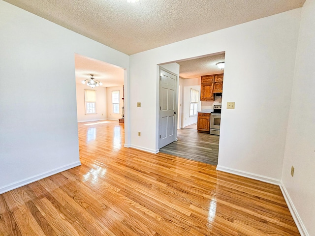 spare room featuring a notable chandelier, wood finished floors, baseboards, and a textured ceiling