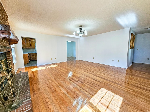 unfurnished living room with a chandelier, light wood-style flooring, a fireplace, and a textured ceiling