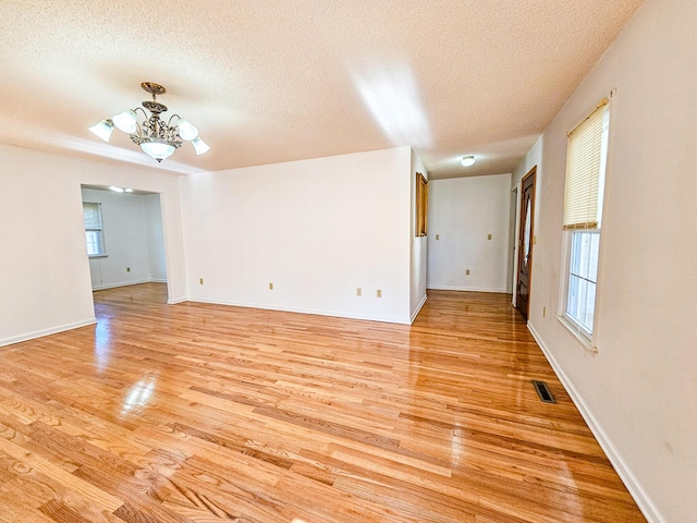 empty room with light wood-type flooring, visible vents, a textured ceiling, and an inviting chandelier