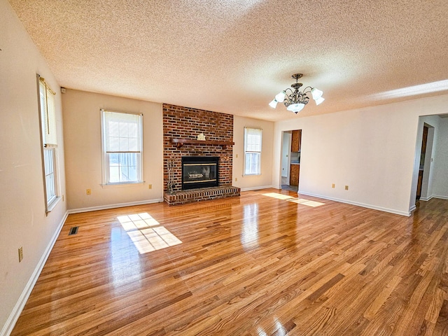 unfurnished living room featuring a fireplace, an inviting chandelier, plenty of natural light, and wood finished floors