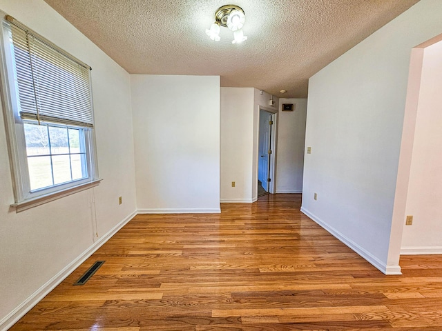 unfurnished room featuring a textured ceiling, light wood-style floors, visible vents, and baseboards