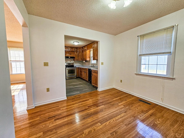 kitchen with light countertops, brown cabinets, stainless steel range with electric cooktop, dark wood-style floors, and a sink