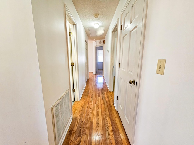 hall with baseboards, visible vents, a textured ceiling, and light wood-style floors