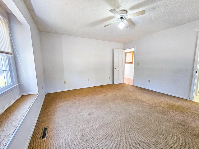 carpeted spare room with visible vents, a textured ceiling, and ceiling fan