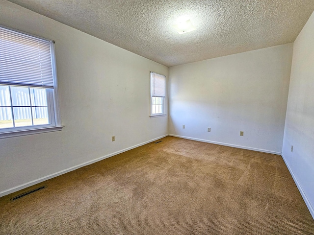 spare room featuring visible vents, baseboards, a textured ceiling, and carpet flooring