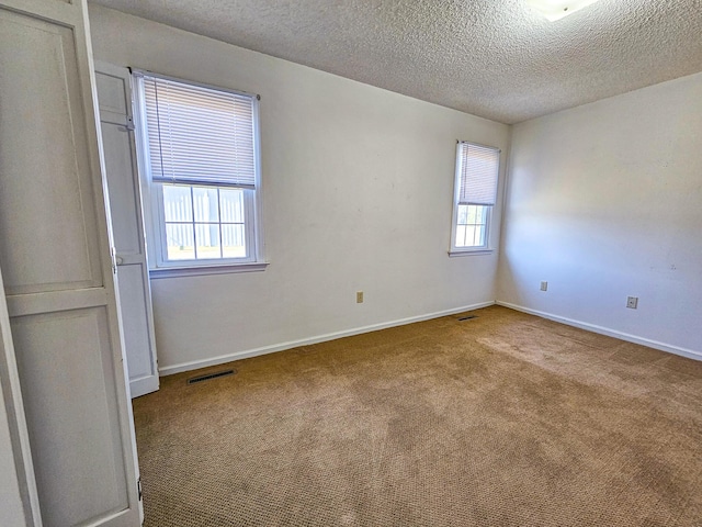 carpeted spare room featuring a healthy amount of sunlight, visible vents, and baseboards