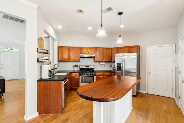 kitchen with stainless steel appliances, a sink, brown cabinetry, light wood-style flooring, and under cabinet range hood