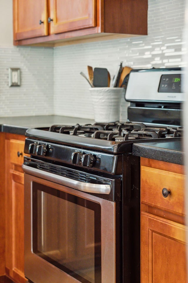 kitchen featuring stainless steel range with gas stovetop, decorative backsplash, dark countertops, and brown cabinetry