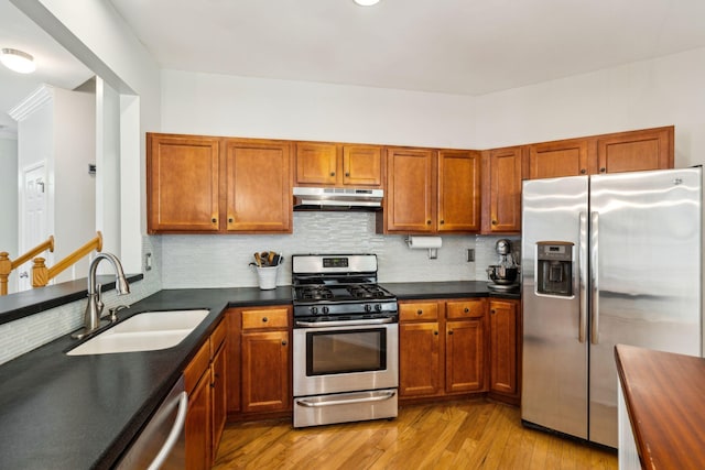 kitchen with stainless steel appliances, a sink, under cabinet range hood, dark countertops, and backsplash