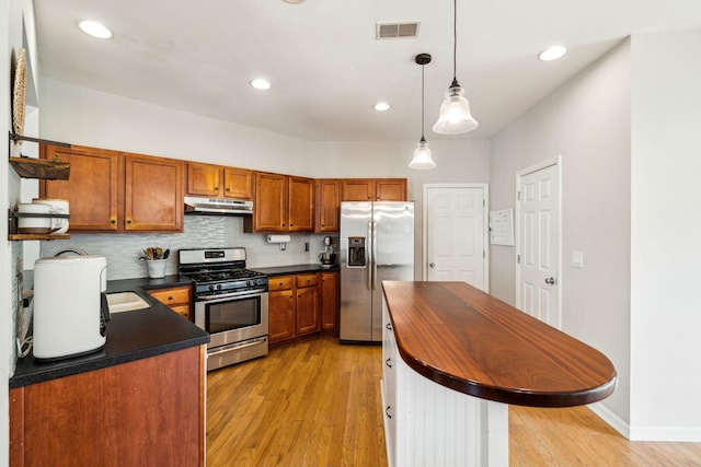 kitchen with stainless steel appliances, under cabinet range hood, light wood finished floors, brown cabinets, and butcher block countertops