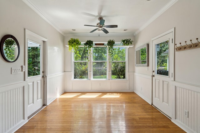 entryway with healthy amount of natural light, a wainscoted wall, ceiling fan, light wood-style flooring, and ornamental molding
