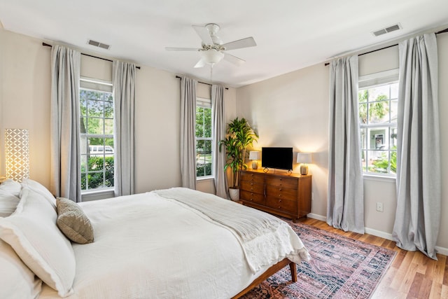 bedroom with multiple windows, wood finished floors, baseboards, and a ceiling fan