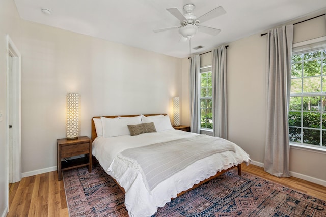 bedroom featuring multiple windows, light wood finished floors, baseboards, and ceiling fan
