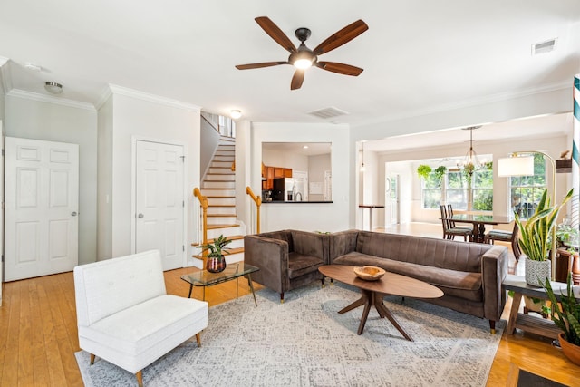 living area with ornamental molding, stairs, ceiling fan, light wood finished floors, and a chandelier