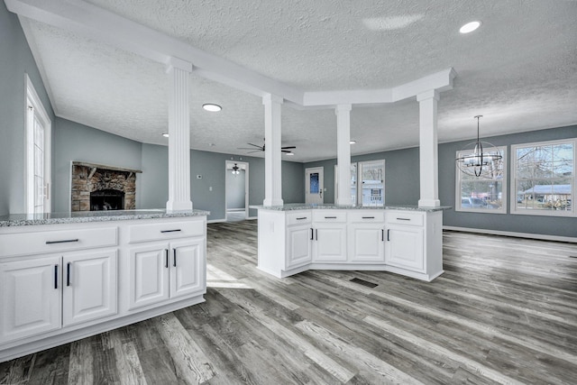 kitchen featuring ceiling fan with notable chandelier, a fireplace, wood finished floors, and decorative columns