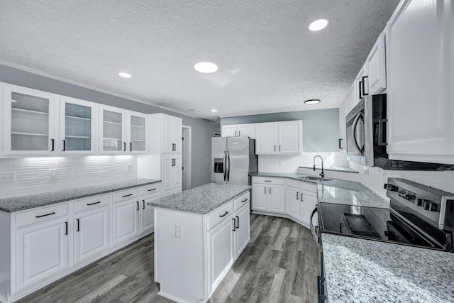 kitchen featuring a kitchen island, wood finished floors, stainless steel appliances, white cabinetry, and a sink