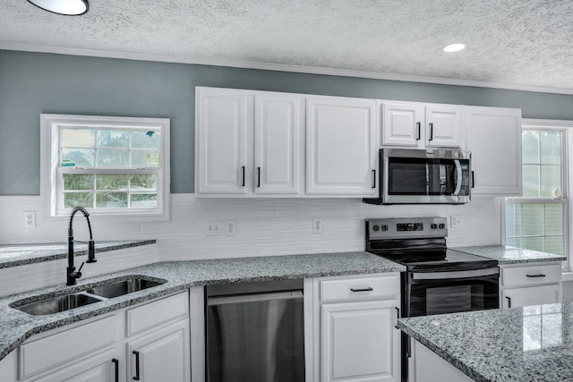 kitchen featuring white cabinets, decorative backsplash, light stone countertops, stainless steel appliances, and a sink