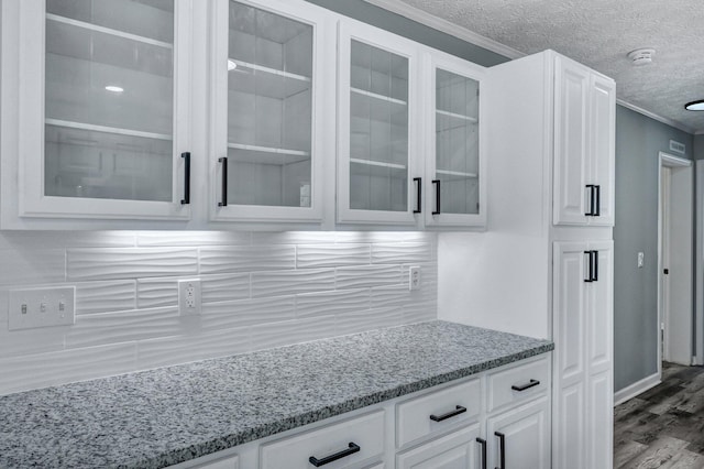 kitchen featuring glass insert cabinets, white cabinets, a textured ceiling, and light stone countertops