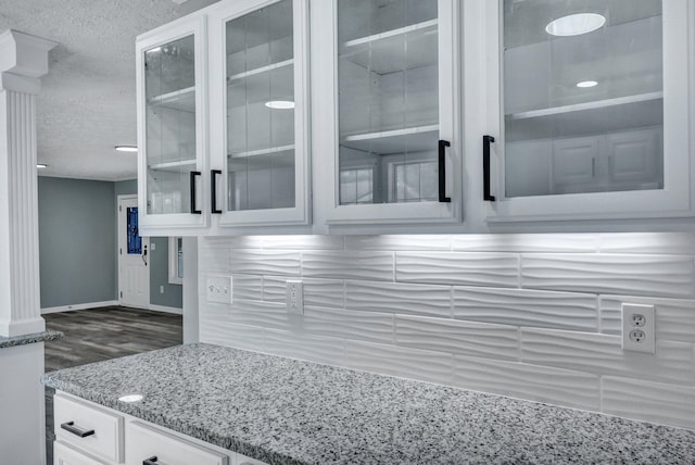 kitchen featuring baseboards, white cabinets, glass insert cabinets, light stone counters, and a textured ceiling