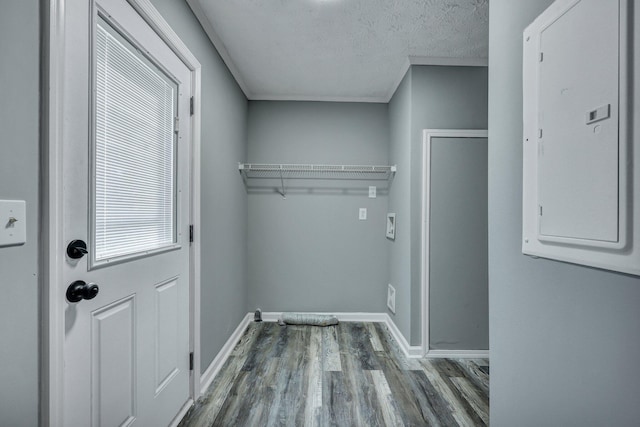 clothes washing area featuring a textured ceiling, electric panel, baseboards, and wood finished floors