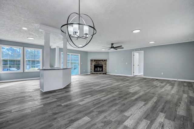 unfurnished living room with baseboards, dark wood-style flooring, a textured ceiling, a stone fireplace, and ceiling fan with notable chandelier