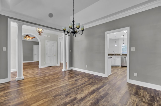 unfurnished dining area featuring dark wood-type flooring, ceiling fan with notable chandelier, sink, crown molding, and ornate columns