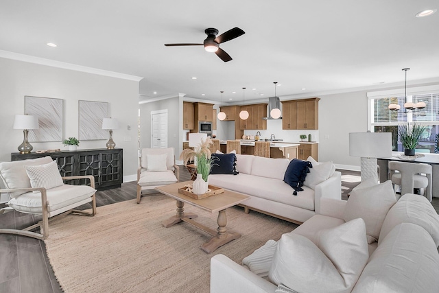 living room with hardwood / wood-style floors, ceiling fan with notable chandelier, ornamental molding, and sink