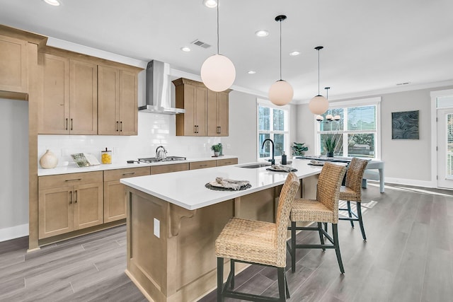 kitchen featuring sink, a breakfast bar area, a kitchen island with sink, hanging light fixtures, and wall chimney exhaust hood