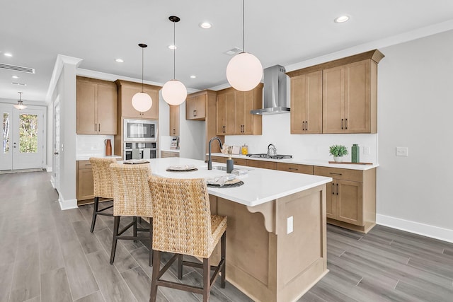 kitchen featuring appliances with stainless steel finishes, sink, a kitchen bar, a kitchen island with sink, and wall chimney range hood