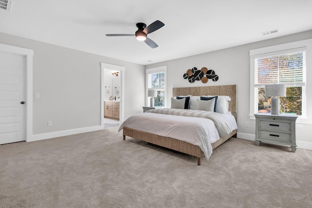 bedroom featuring ceiling fan, light colored carpet, and ensuite bath