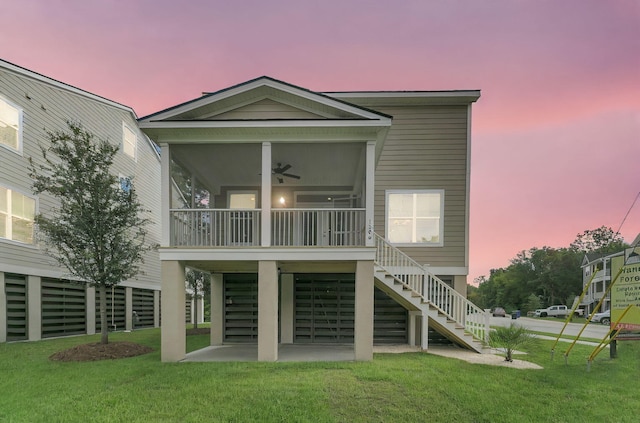 back house at dusk with a patio, a sunroom, ceiling fan, and a lawn