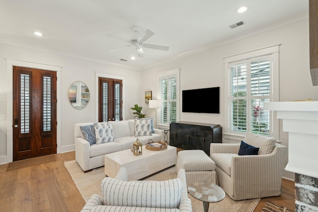 living room with visible vents, light wood-style flooring, a ceiling fan, and ornamental molding