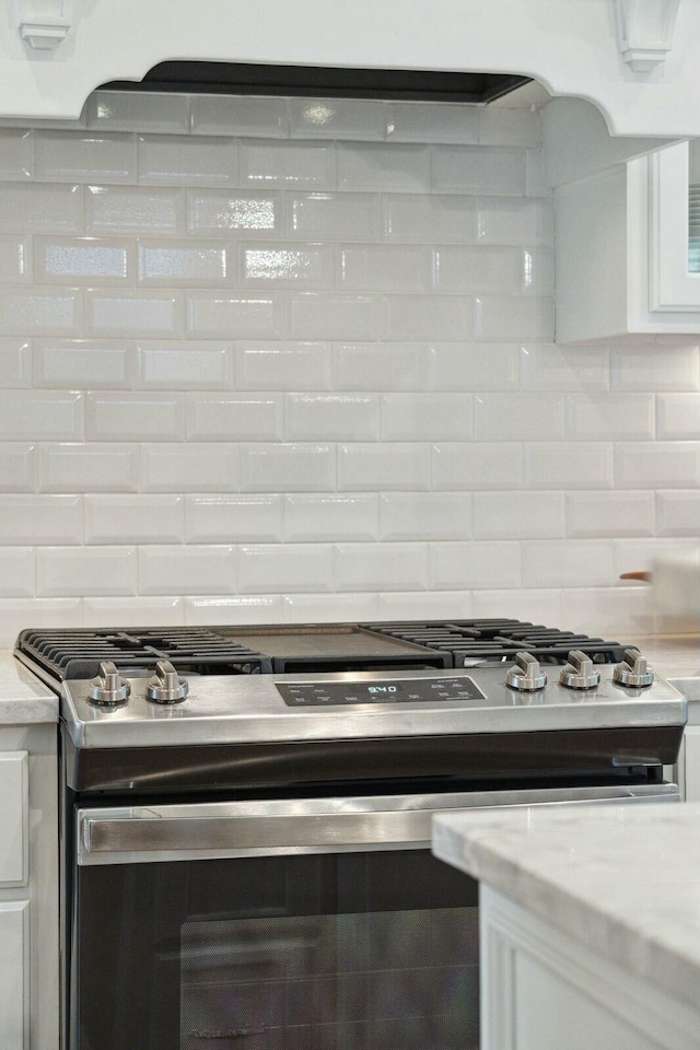 kitchen featuring tasteful backsplash, stainless steel range with gas stovetop, and white cabinets