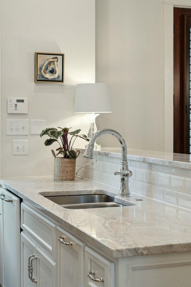 interior details featuring light stone counters, white cabinetry, and a sink