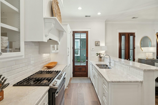 kitchen with visible vents, stainless steel gas stove, a sink, light wood finished floors, and glass insert cabinets