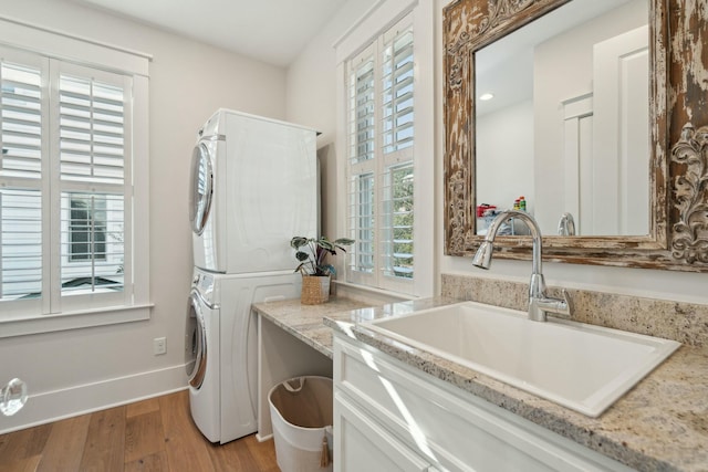 laundry area featuring light wood finished floors, stacked washer / dryer, baseboards, and a sink