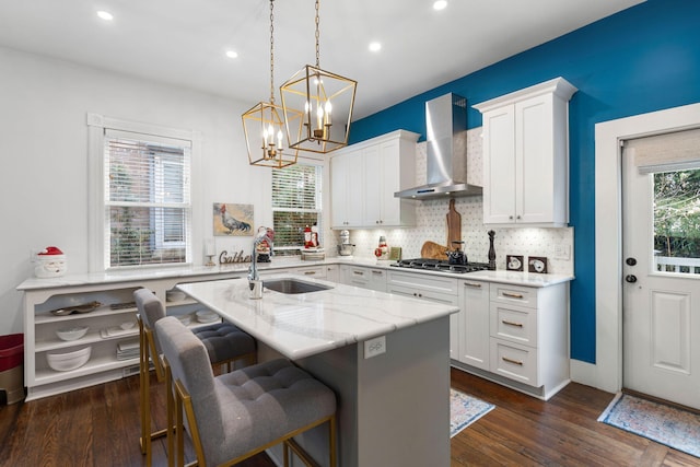 kitchen featuring white cabinetry, sink, wall chimney exhaust hood, a kitchen breakfast bar, and light stone counters