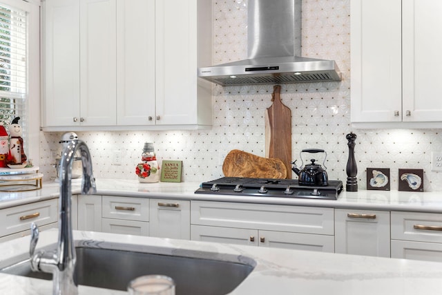 kitchen with backsplash, white cabinetry, sink, and wall chimney range hood