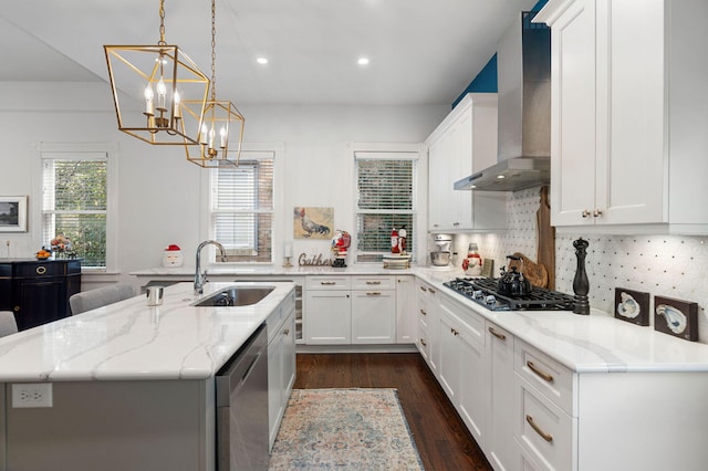 kitchen featuring white cabinets, an island with sink, wall chimney range hood, and appliances with stainless steel finishes