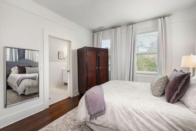 bedroom featuring ensuite bath, dark hardwood / wood-style flooring, and multiple windows