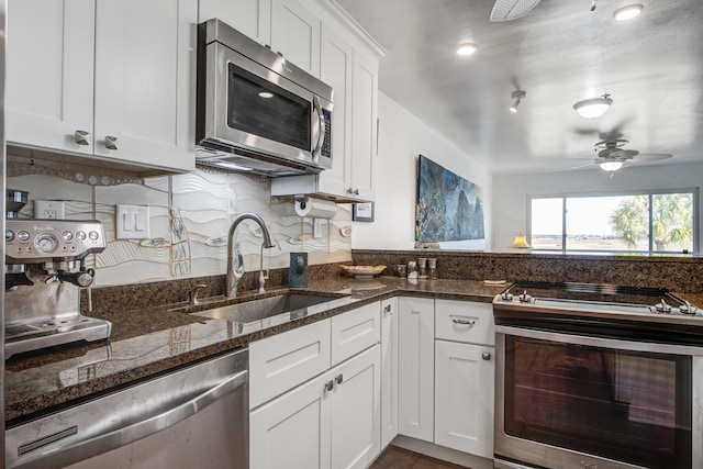 kitchen with a ceiling fan, dark stone counters, a sink, stainless steel appliances, and white cabinets