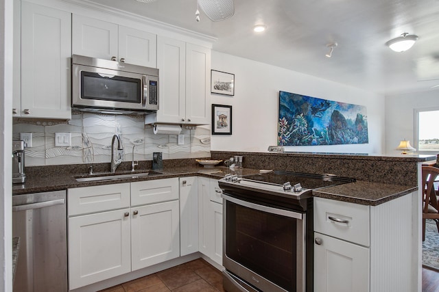 kitchen featuring a peninsula, a sink, stainless steel appliances, white cabinets, and dark tile patterned floors