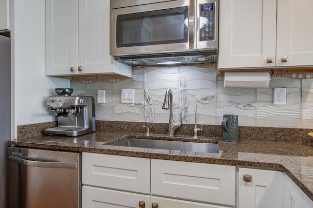 kitchen with a sink, dark stone counters, appliances with stainless steel finishes, and white cabinetry