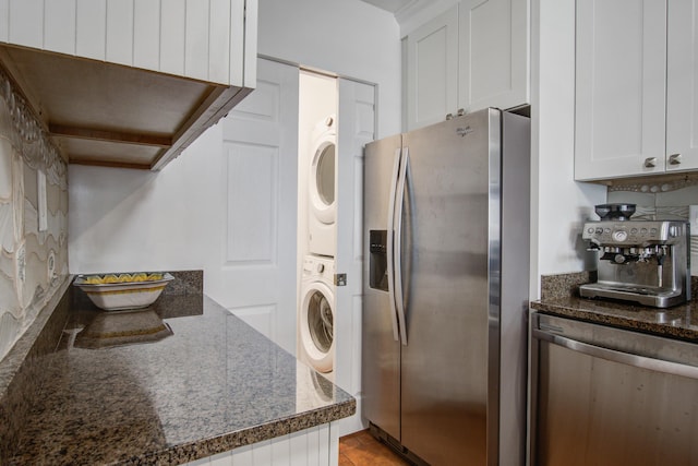 kitchen with dark stone countertops, white cabinets, stainless steel fridge with ice dispenser, and stacked washing maching and dryer