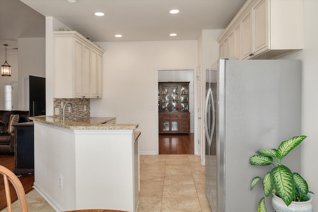 kitchen featuring kitchen peninsula, stainless steel fridge, tasteful backsplash, light stone countertops, and light hardwood / wood-style floors