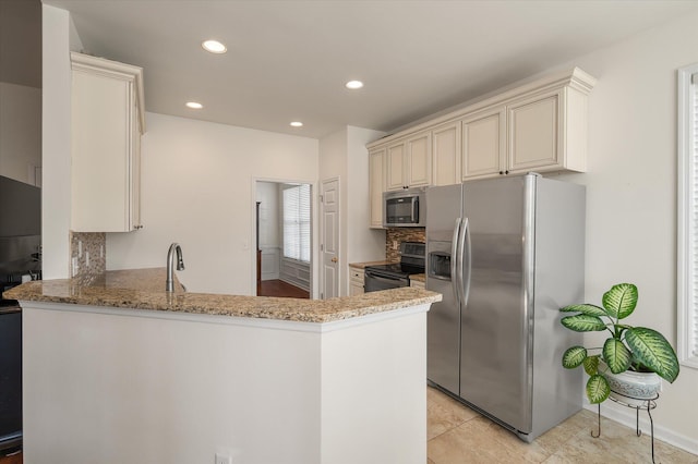 kitchen featuring appliances with stainless steel finishes, kitchen peninsula, light stone countertops, and cream cabinetry