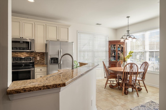 kitchen with decorative backsplash, appliances with stainless steel finishes, a chandelier, cream cabinetry, and light stone counters