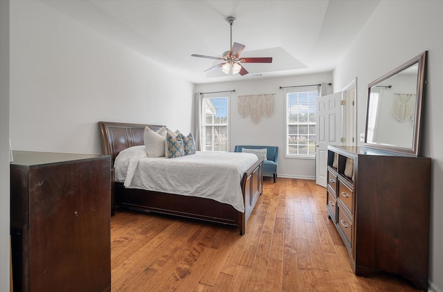 bedroom with a tray ceiling, light wood-type flooring, and ceiling fan