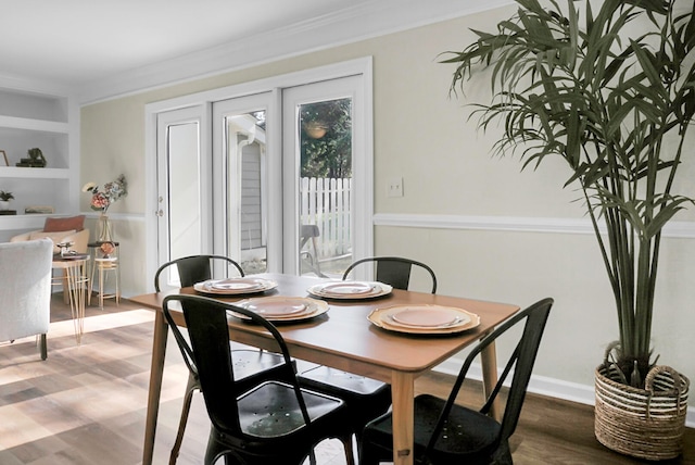 dining space with wood-type flooring, built in features, and crown molding